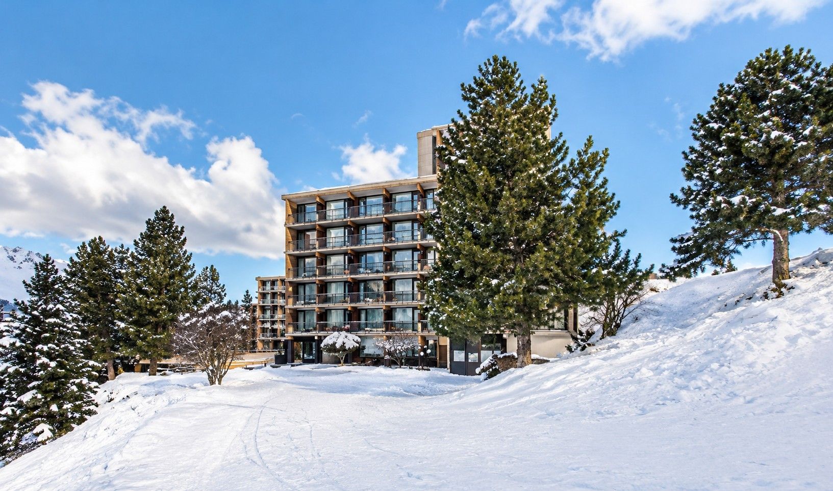 A multi-story hotel with a modern design, surrounded by snow-covered trees and a clear sky.
