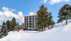 A multi-story hotel with a modern design, surrounded by snow-covered trees and a clear sky. - Apartment '- Les 2 Alpes' with Mountain View, Shared Pool and Wi-Fi (Les Deux Alpes)