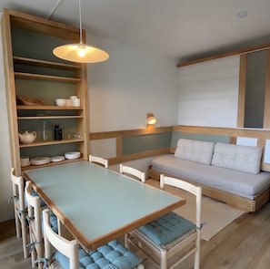 A compact living space with a dining table, chairs, a sofa with cushions, a shelf with kitchenware, and a hanging light fixture. - Apartment '- Les 2 Alpes' with Mountain View, Shared Pool and Wi-Fi (Les Deux Alpes)
