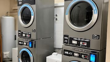 Two stacked commercial washing machines with digital displays, a water tank, and a white tiled wall.
