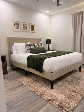 Une chambre à coucher avec un lit, une table de chevet, une lampe et des tableaux encadrés accrochés au mur.