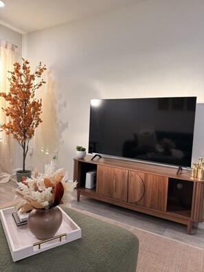 Un salon moderne avec un téléviseur à écran plat, un meuble de rangement en bois, des plantes décoratives et un plateau sur lequel est posé un vase.