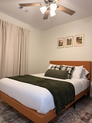 Ein Schlafzimmer mit einem Bett, einem Deckenventilator und drei gerahmten Bildern an der Wand.
