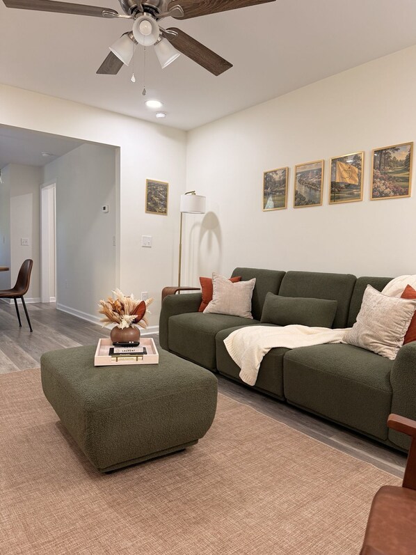 Ein modernes Wohnzimmer mit einem Ecksofa, einem Couchtisch, einer Stehlampe und gerahmten Kunstwerken an der Wand.
