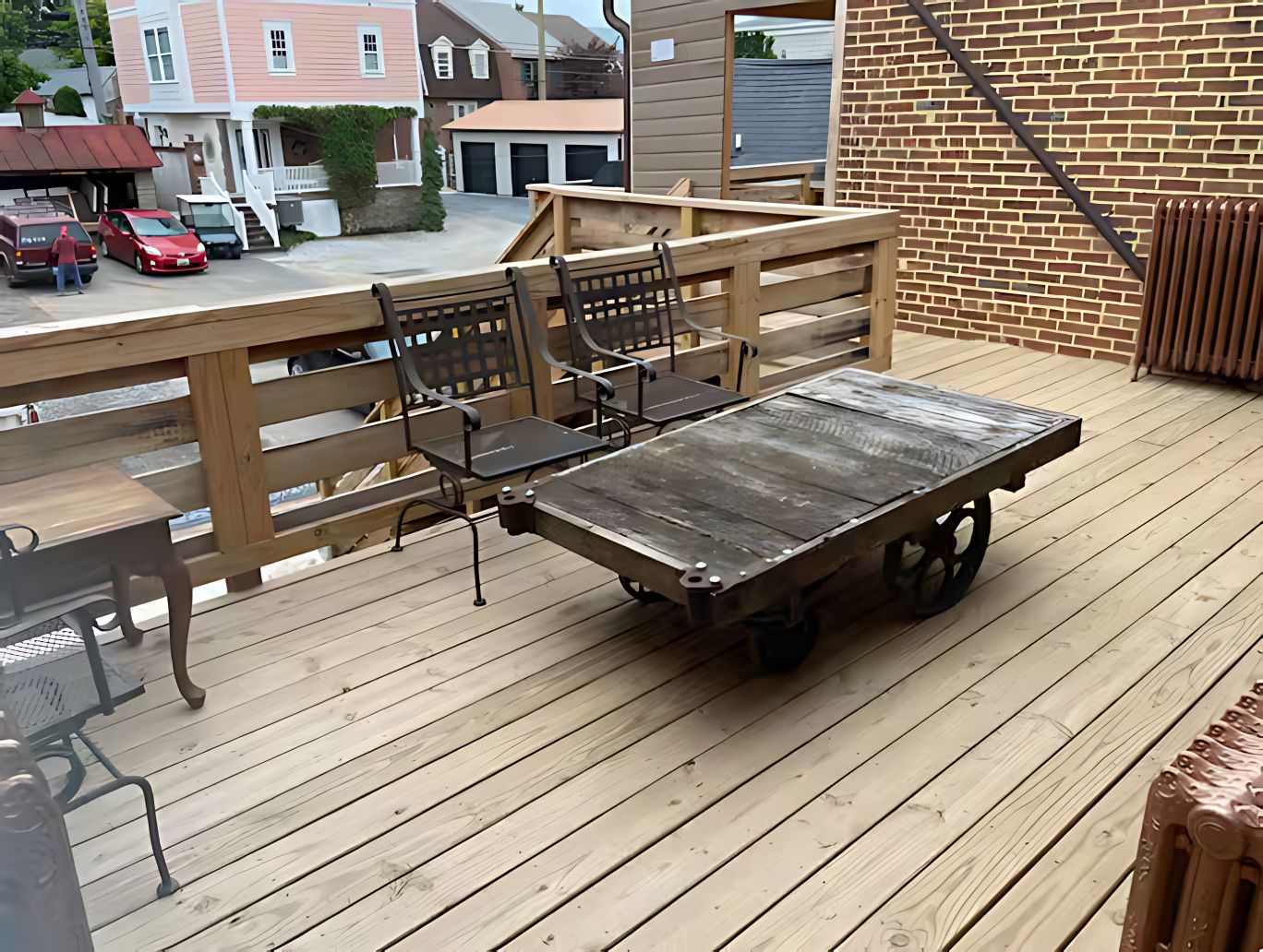 Una terraza de madera con una mesa y sillas, un muro de ladrillo y vistas a casas al fondo.