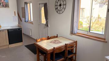 Una zona de menjador amb taula i cadires de fusta, un rellotge a la paret i una finestra amb cortines.