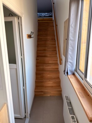 Un pasillo estrecho con una escalera de madera que lleva a una habitación con ventana.