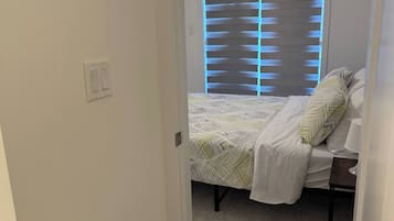 A bedroom with a bed, a nightstand, a lamp, and a window with blinds.