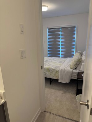 Quarto com cama, mesa de cabeceira, luminária e janela com persianas.