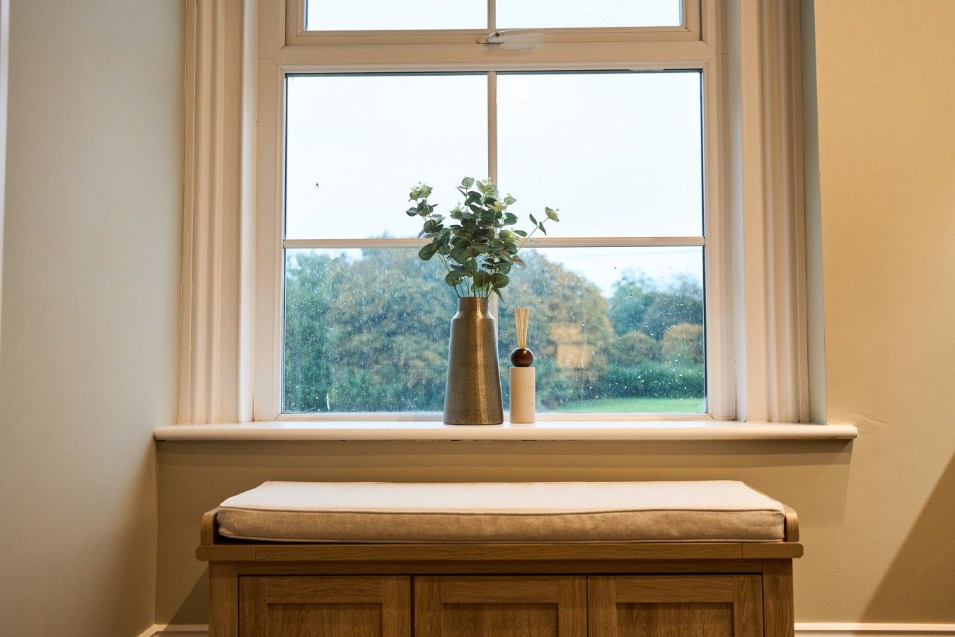 A window with a view of trees and a bench below.