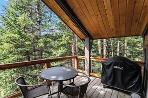 Une terrasse extérieure couverte, dotée d’une table et de chaises, et entourée d’arbres.