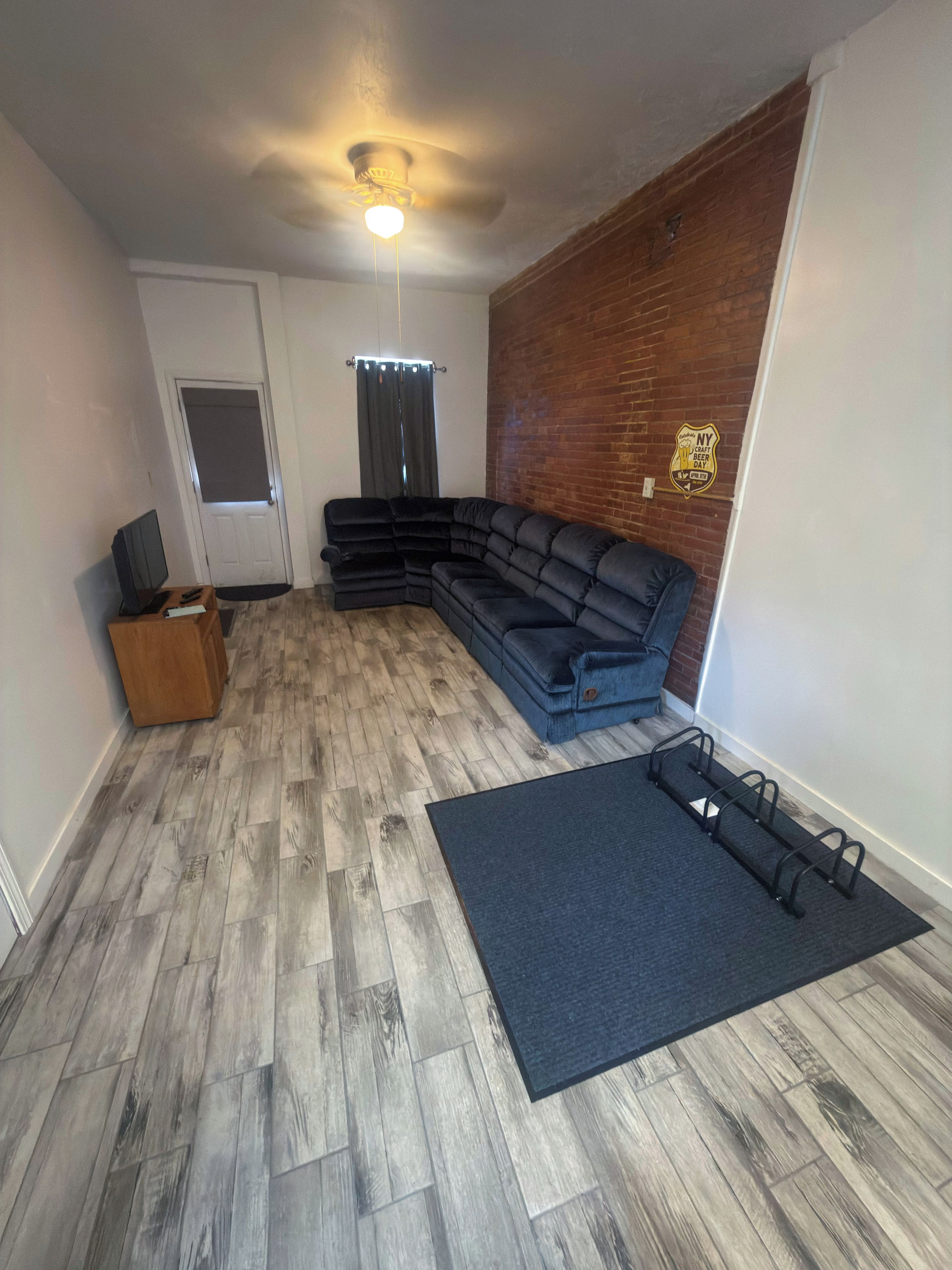 Una sala de estar con sofá modular, piso de madera, ventilador de techo y pared de ladrillo decorativa.