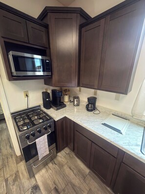 A compact kitchen with dark wooden cabinets, a stainless steel stove, a microwave, and a coffee maker. - 1BR close to the Erie Canal Trail, and across from Lunkenheimer Craft Brewery (Weedsport)