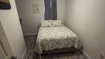 Een klein appartement met één kamer, een bed, een raam met gordijnen, een deur en een plafondlamp.