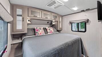 A bedroom with a bed, cabinets, a window, and a ceiling vent.