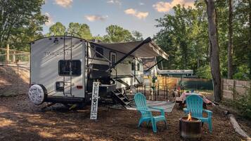 A TWILIGHT RV with a covered patio area, two turquoise Adirondack chairs, and a campfire.