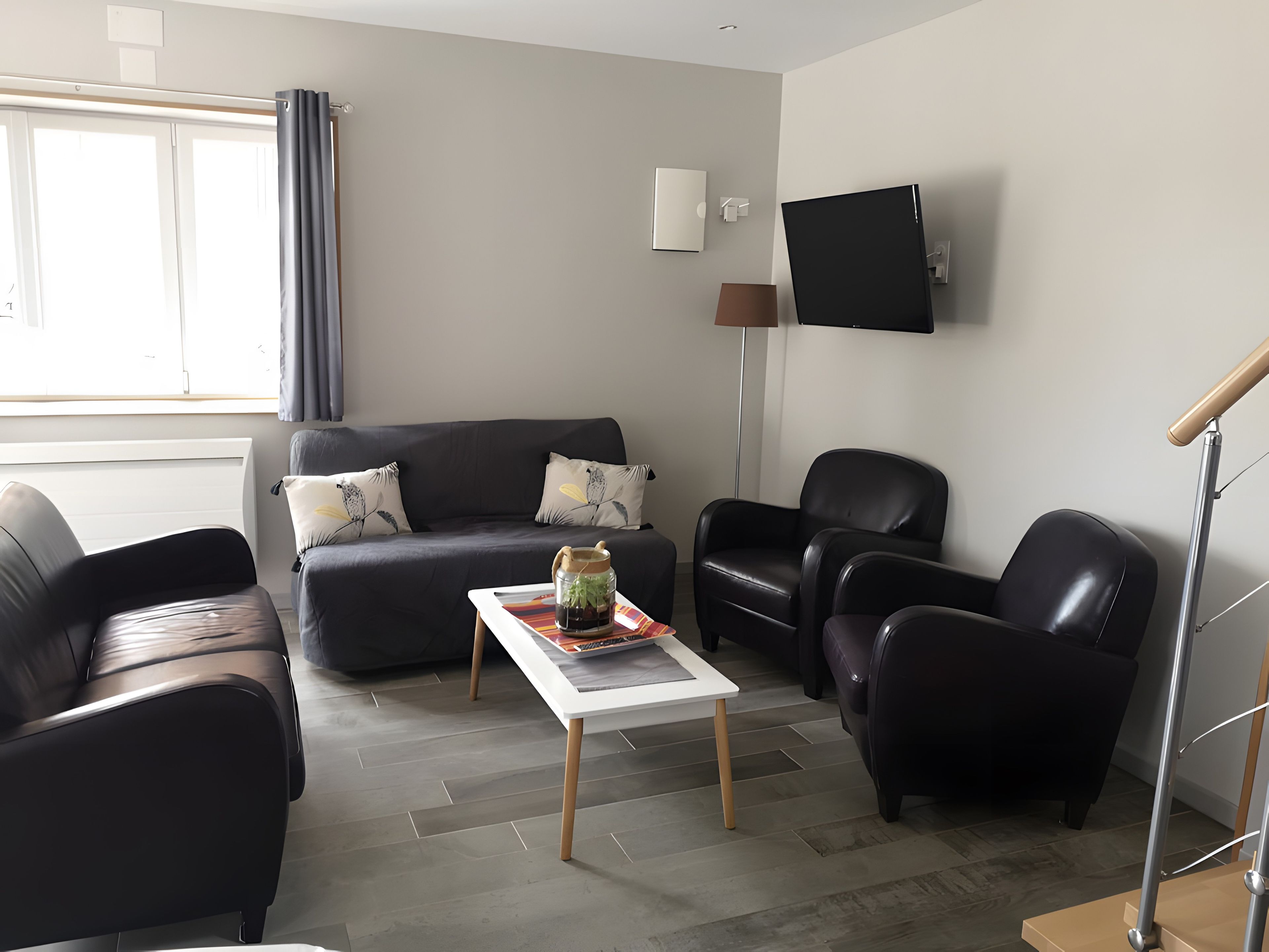 A modern living room with a sofa, two armchairs, a coffee table, and a flat-screen TV mounted on the wall.