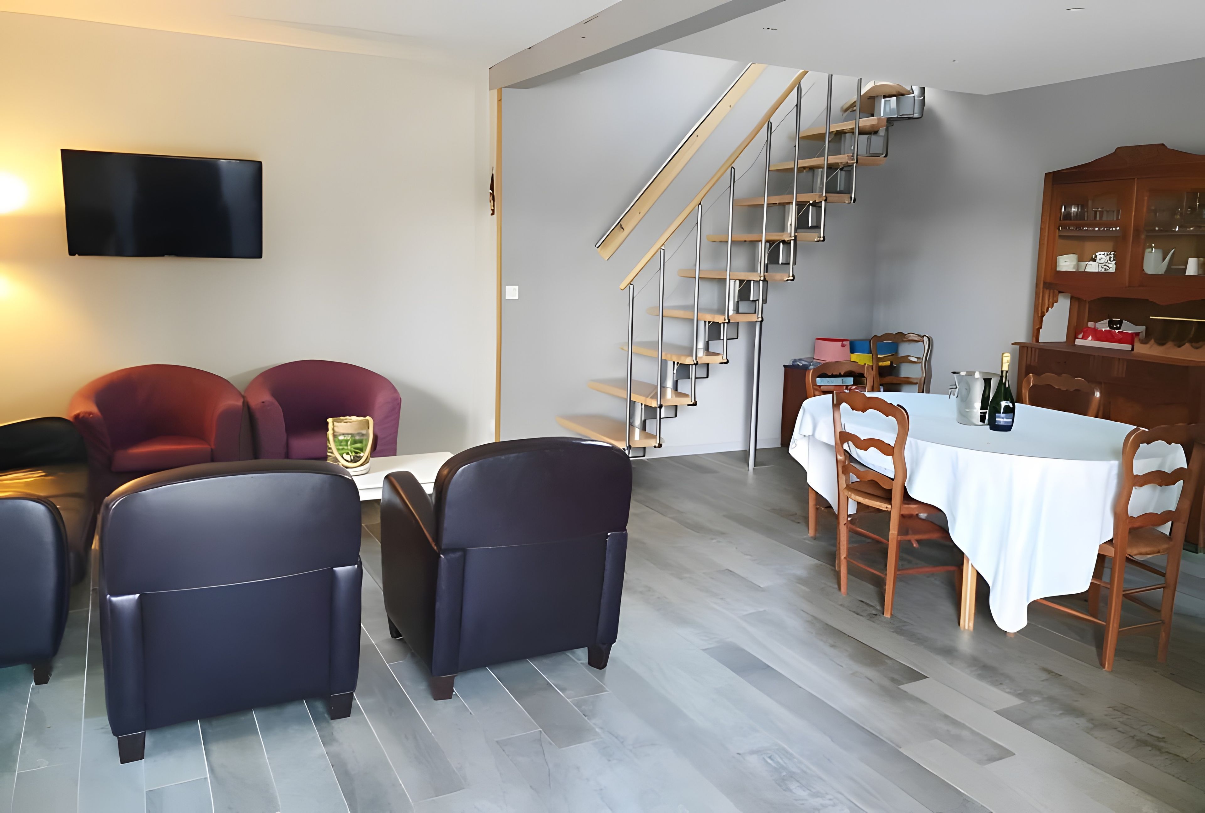 A modern living room with a dining area, a staircase, and a flat-screen TV.
