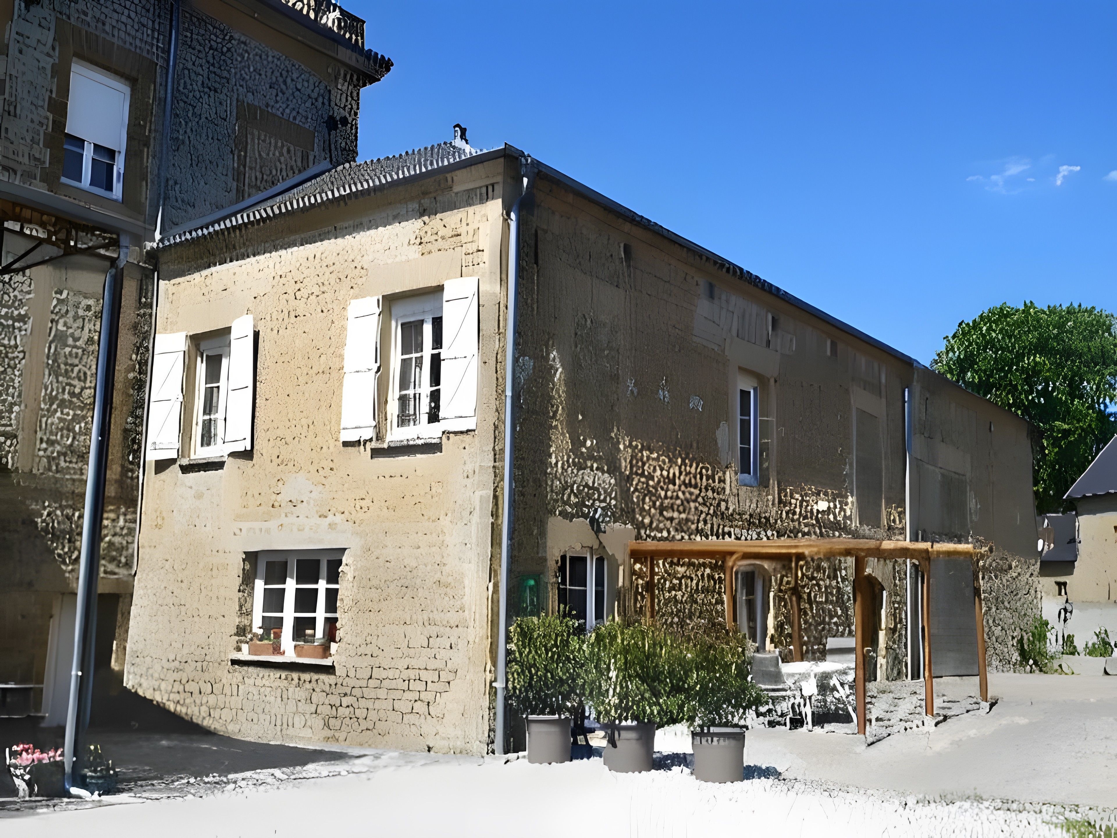A two-story building with a stone facade, multiple windows with shutters, and a covered outdoor seating area with potted plants.