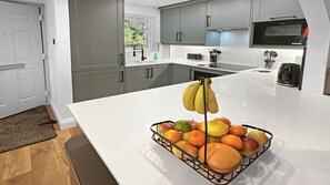 Una cocina moderna con armarios grises, encimera blanca y una cesta de frutas con plátanos y naranjas.