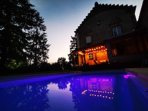 Un bâtiment doté d’une piscine dont l’eau reflète les lumières, entouré d’arbres.