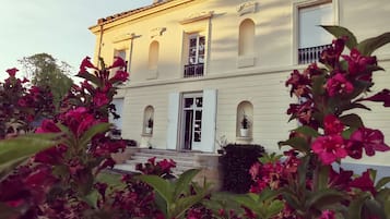 Un bâtiment à deux étages doté d’une façade symétrique, d’une entrée centrale avec une porte et d’un balcon au deuxième étage.