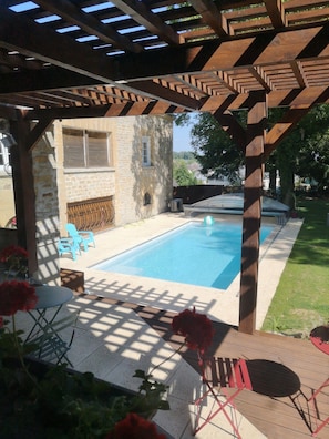 A covered outdoor swimming pool with a stone wall, wooden deck, and a pergola overhead. - Bed and Breakfast 'Ma Boheme' with Shared Pool, Shared Terrace and Wi-Fi (Tournes)