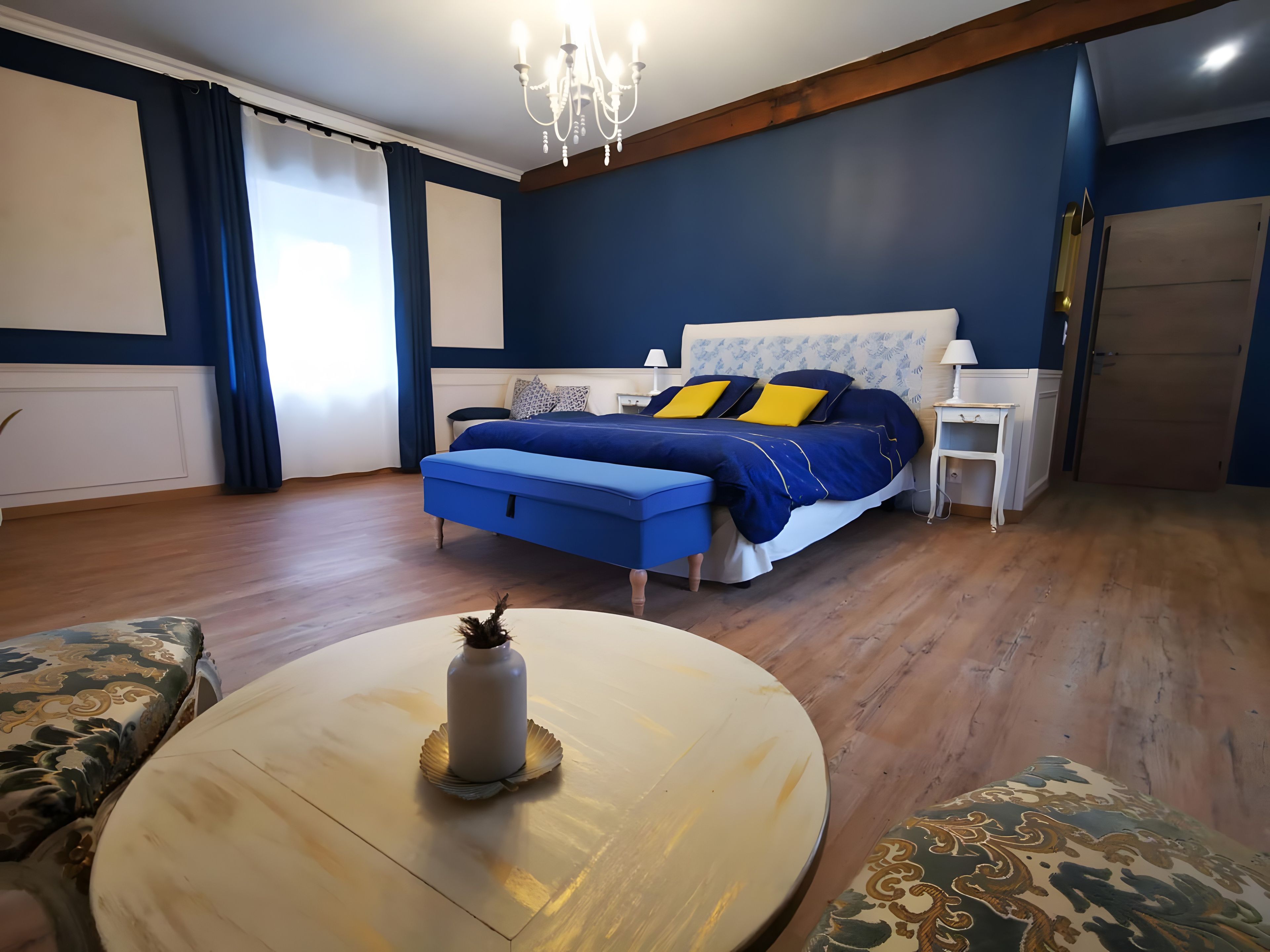 A bedroom with a bed, bedside tables, a round table, and a chandelier.