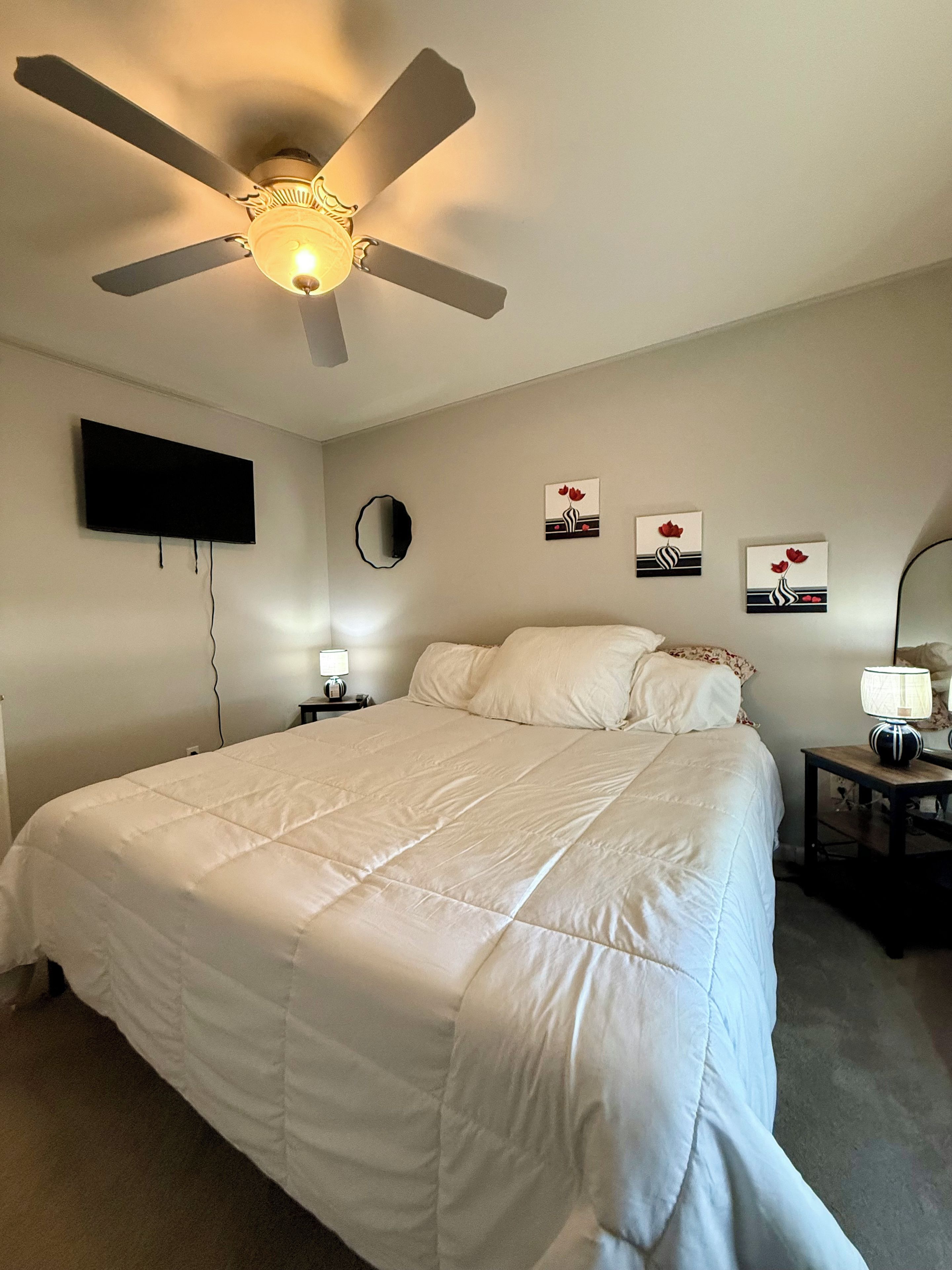 Ein Schlafzimmer mit einem Bett, einem Deckenventilator, einem Flachbildfernseher und Wandbildern.
