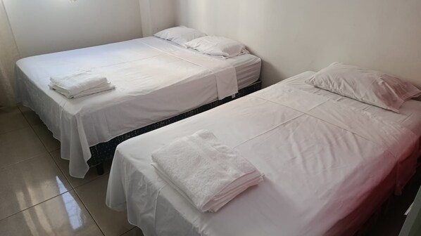 Two single beds with white linens and pillows, a tiled floor, and a plain white wall. - New Listing (Salinas)