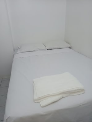 A small, white, single-bed room with a neatly made bed and a folded white towel on the bed. - New Listing (Salinas)