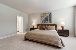 A bedroom with a large bed, two bedside tables, a nightstand, a door leading to another room, and a wall-mounted abstract painting. - Spacious Raleigh Retreat with King Suite, Workspace & Sleeps 6 (Raleigh)