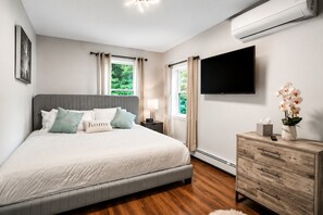 Bright Bedroom with TV — Comfortable bedroom with natural light, fresh linens, storage, and a flat-screen television.