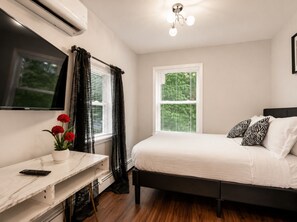 A bedroom with a bed, a TV, a desk, and a window with blinds.