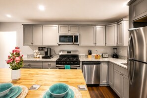 A modern kitchen with grey cabinets, stainless steel appliances, and a wooden dining table with teal plates.