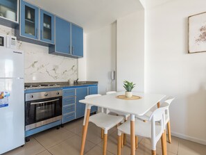 A modern kitchen with blue cabinets, a white countertop, and a dining table with white chairs. - Bright and comfortable apartment in Congreso (Buenos Aires)