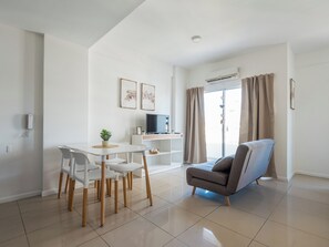 Un salon moderne comprenant un coin repas, un canapé gris, un téléviseur et une porte-fenêtre coulissante.