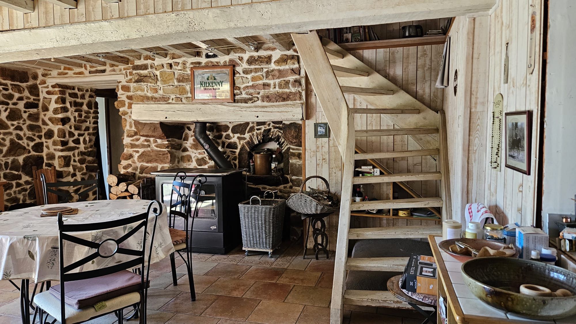 Un intérieur rustique avec un mur en pierre, un escalier en bois et une table entourée de chaises.