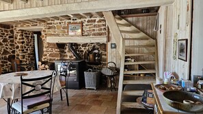 Un interno rustico con parete in pietra, scala in legno e tavolo con sedie.