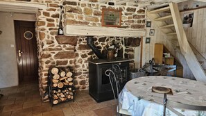 Une pièce rustique avec un mur en pierre, une porte en bois, une cheminée ornée d’une enseigne de la bière irlandaise Kilkenny, une table recouverte d’une nappe à motifs floraux et un escalier en bois.
