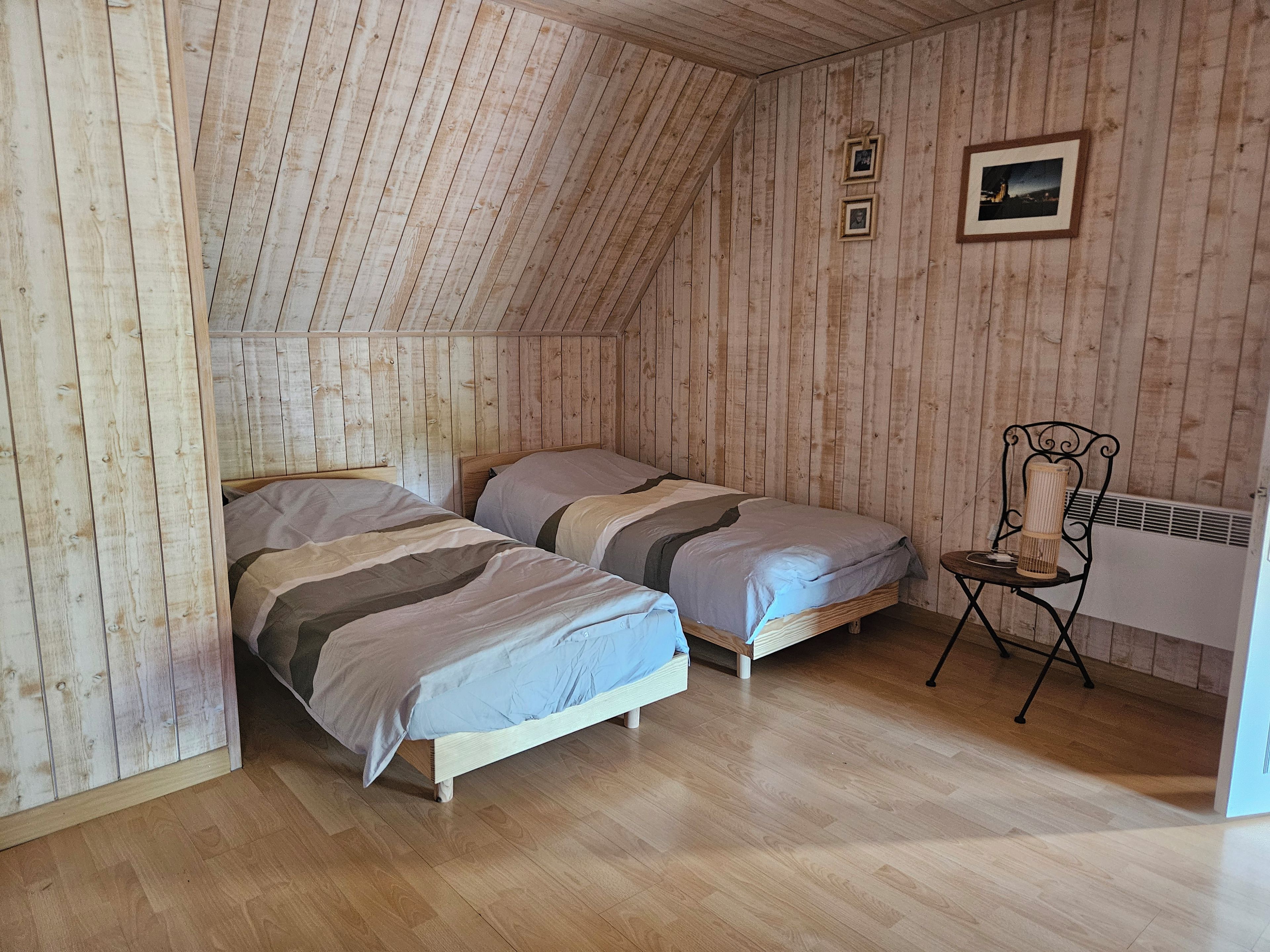 Quarto com duas camas, paredes de madeira e uma cadeira.