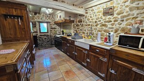 Une cuisine avec des murs en pierre, des armoires en bois, un évier et un four à micro-ondes.