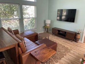 A living room with a sofa set, a wooden coffee table, a TV mounted on the wall, and a small lamp on a side table. - Charming 3-bedroom house with AC in lovely Three Rivers (Three Rivers)
