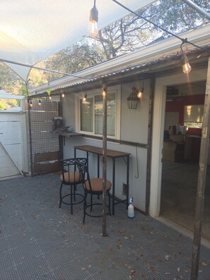 A covered outdoor seating area with a table and chairs, a hanging light fixture, and a view of the house interior. - Charming 3-bedroom house with AC in lovely Three Rivers (Three Rivers)