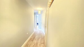 Un couloir avec un plancher en bois, un luminaire et une porte au fond.