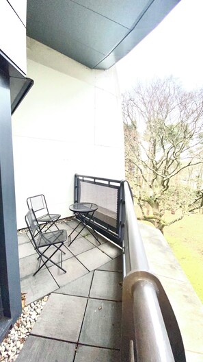 Un balcon avec une table et deux chaises, un mur en pierre et un arbre en arrière-plan.