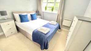Quarto de hotel com cama, mesas de cabeceira, guarda-roupa e janela com cortinas.