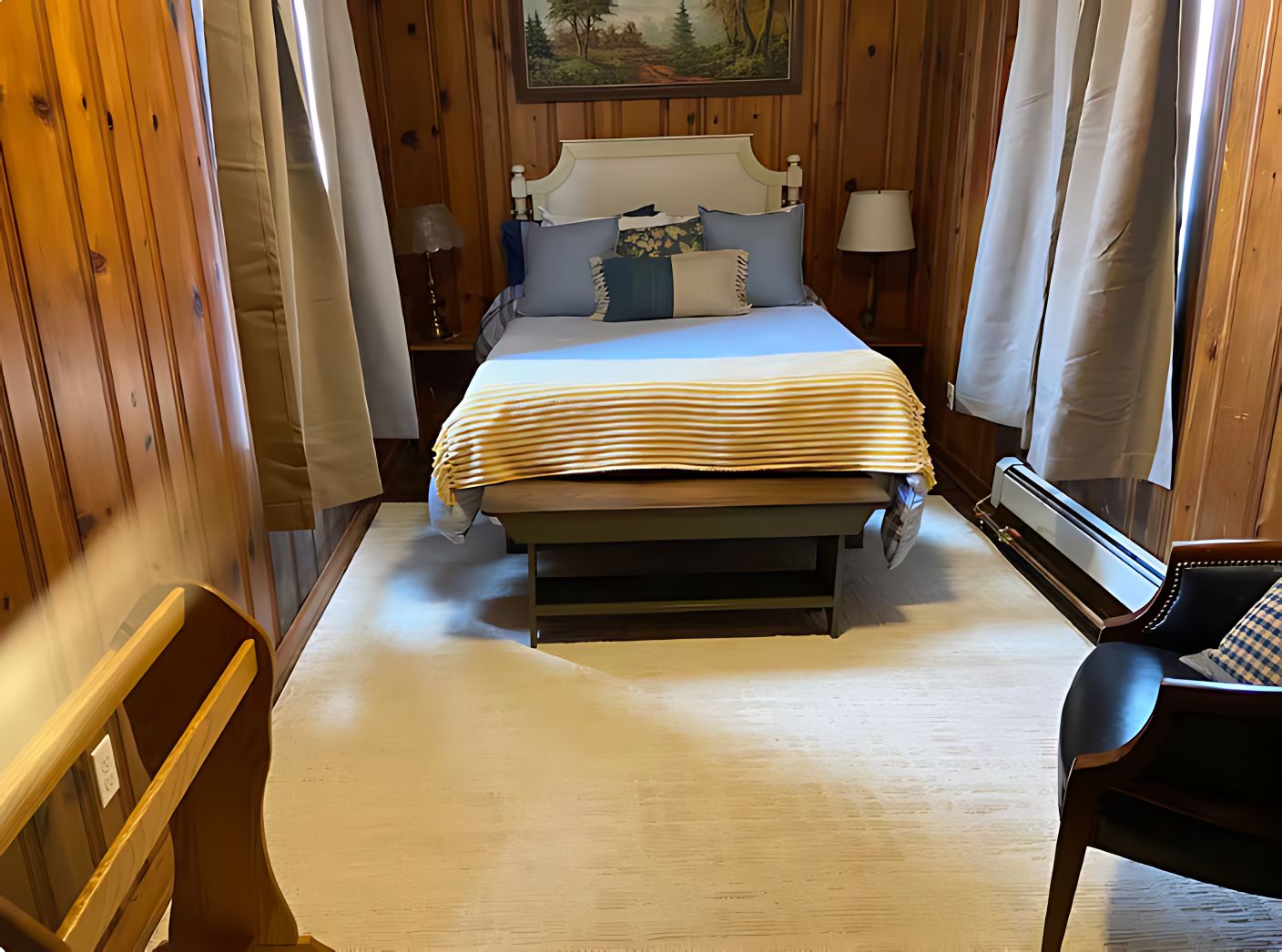 Un dormitorio con cama, lámparas de noche, una silla y un cuadro en la pared.