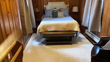 Un dormitorio con cama, lámparas de noche, una silla y un cuadro en la pared.
