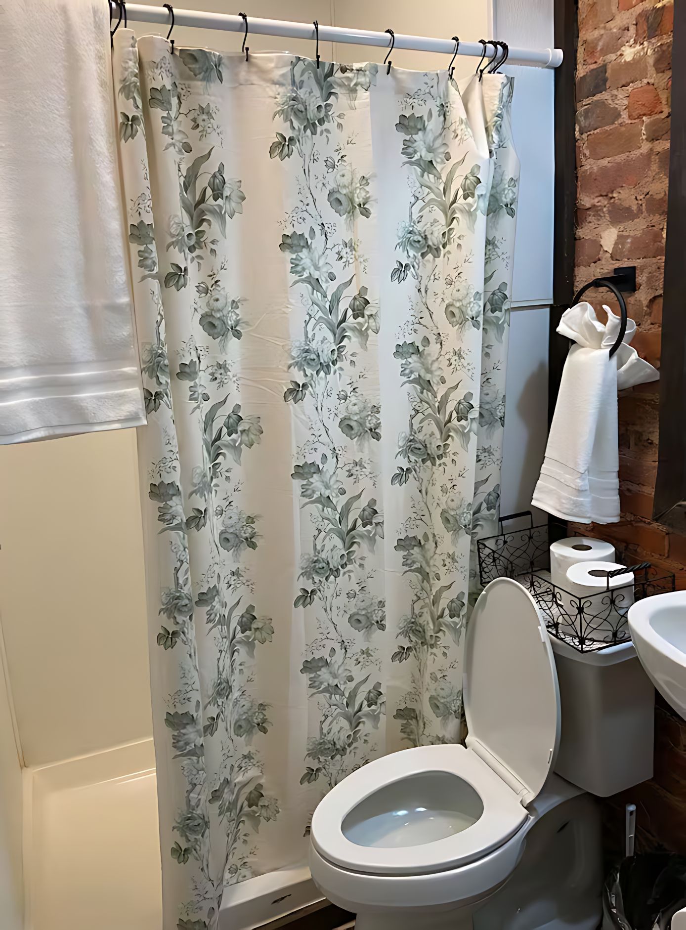 Un baño con inodoro, cortina de ducha con motivos florales, toallero y pared de ladrillo.